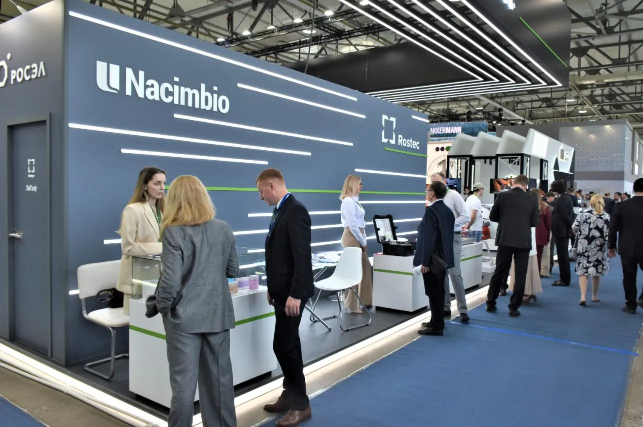 Серый стенд Nacimbio с белыми буквами, горизонтальными световыми линиями и подсветкой по краю подиума.