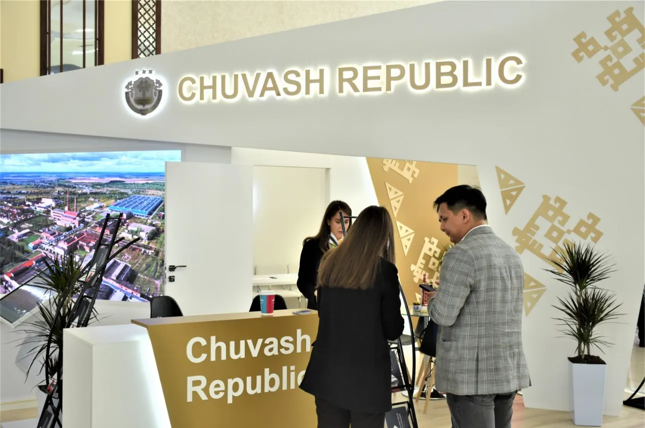 Белый стенд Chuvash Republic с крупной светящейся надписью, золотистым орнаментом и стойкой ресепшен.